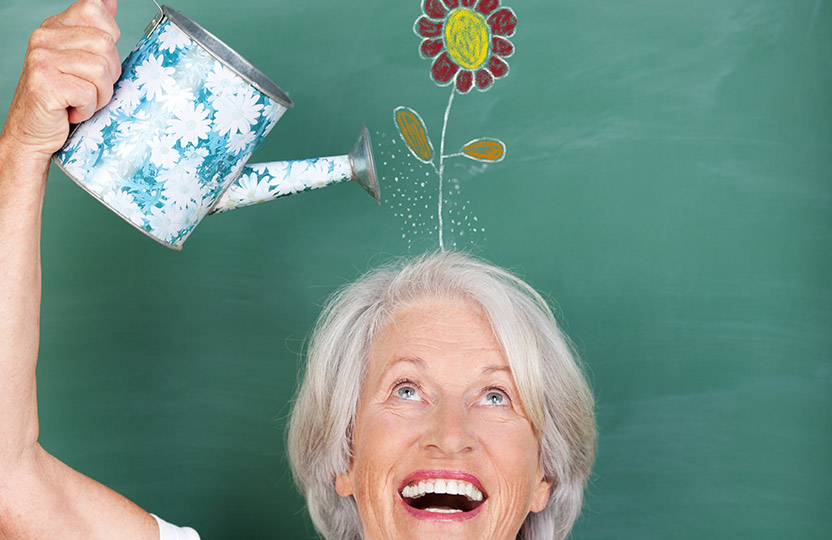 Lächelnde Seniorin gießt symbolisch eine auf eine Tafel gemalte Blume über ihrem Kopf