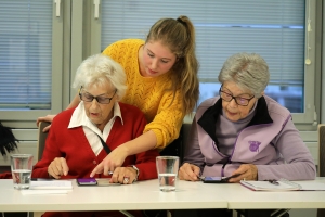 Zwei Kursteilnehmerinnen schauen auf ihre Smartphones. Eine Internetpatin steht hinter ihnen.