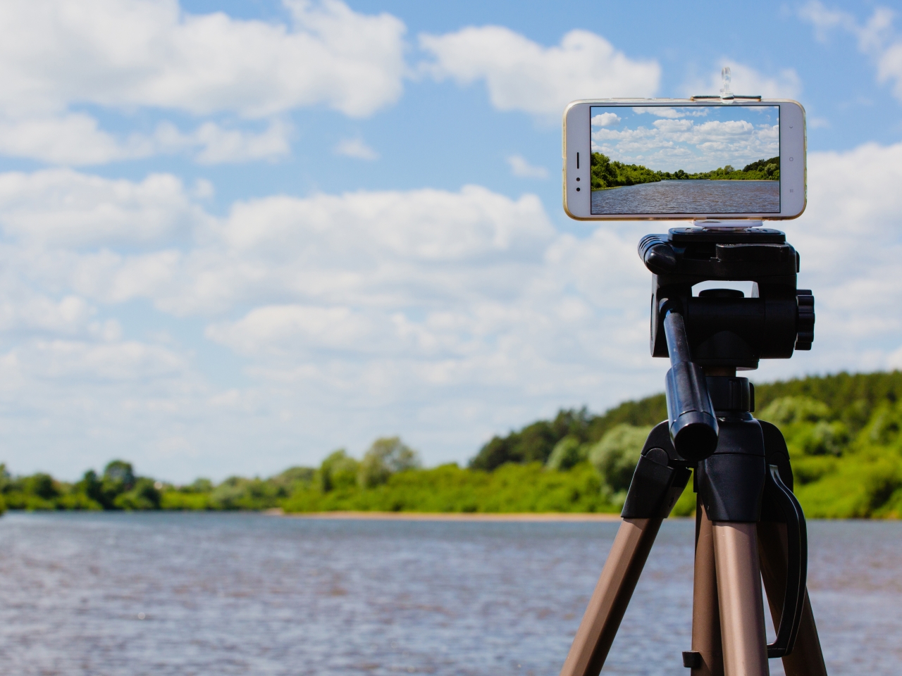 Ein Smartphone ist auf einem Stativ befestigt. Im Hintergrund eine Naturlandschaft