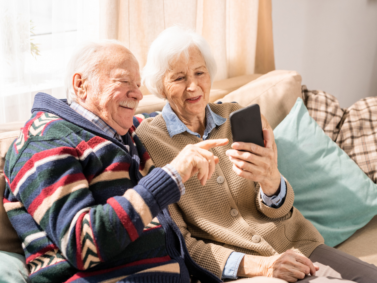 Älteres Paar sitzt auf der Couch und viedeoteefoniert über ein Smartphone