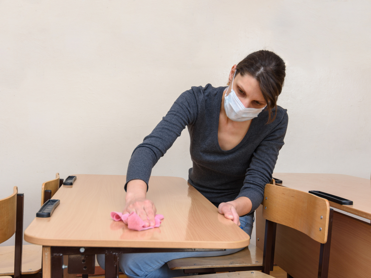 Frau desinfiziert Schreibtisch und trägt dabei eine Maske