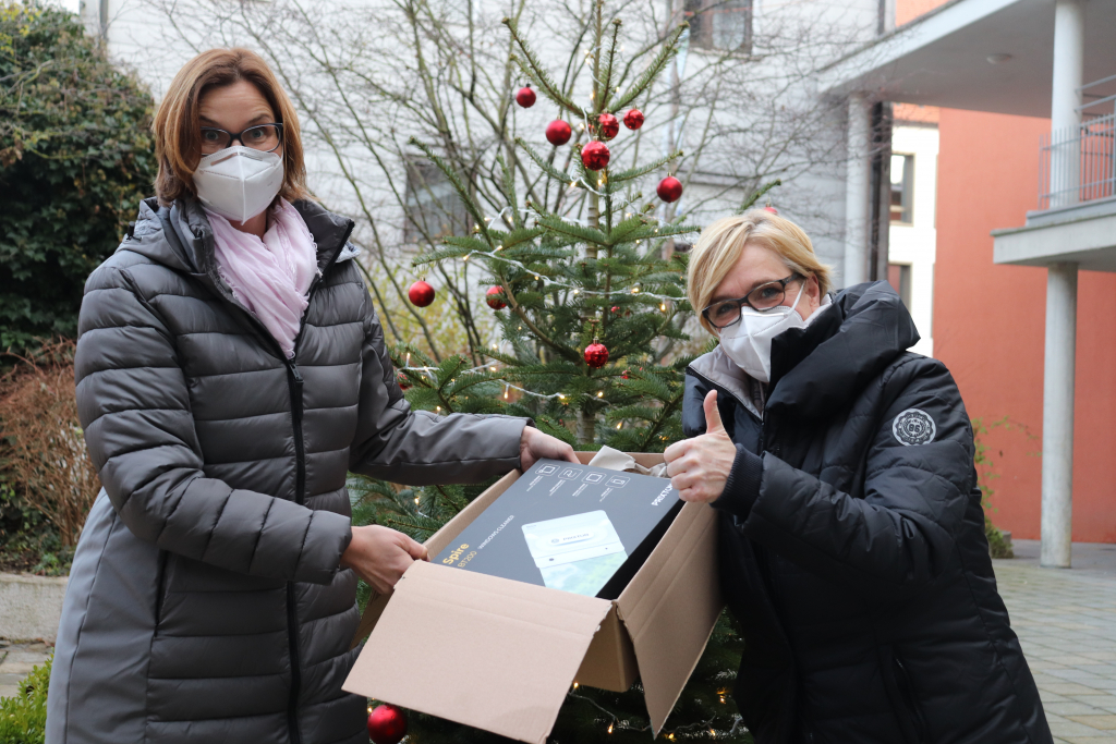 Zwei Frauen halten vor einem Weihnachtsbaum ein Paket