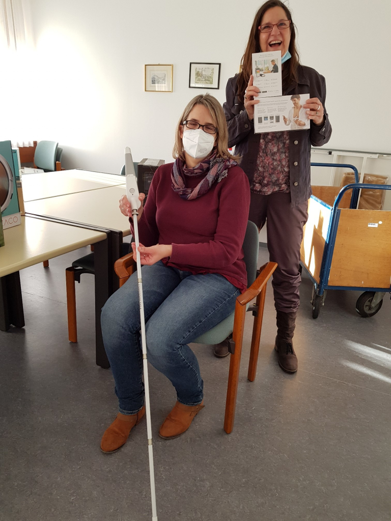 Zwei Frauen präsentieren eine Gehilfe für Sehbeeinträchtigte und ein EKG-Messgerät