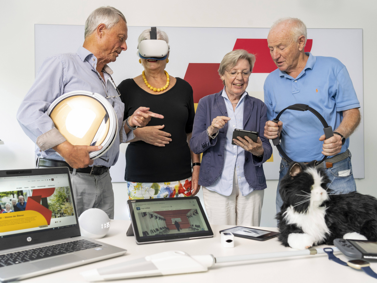 Vier ältere Menschen testen verschiedene digitale Geräte