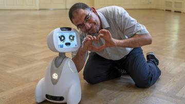 Mann hockt neben einem Roboter und formt mit den Händen ein Herz