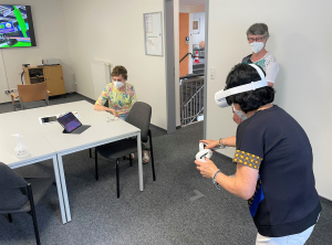 Frau spielt mit VR-Brille, zwei Frauen schauen zu