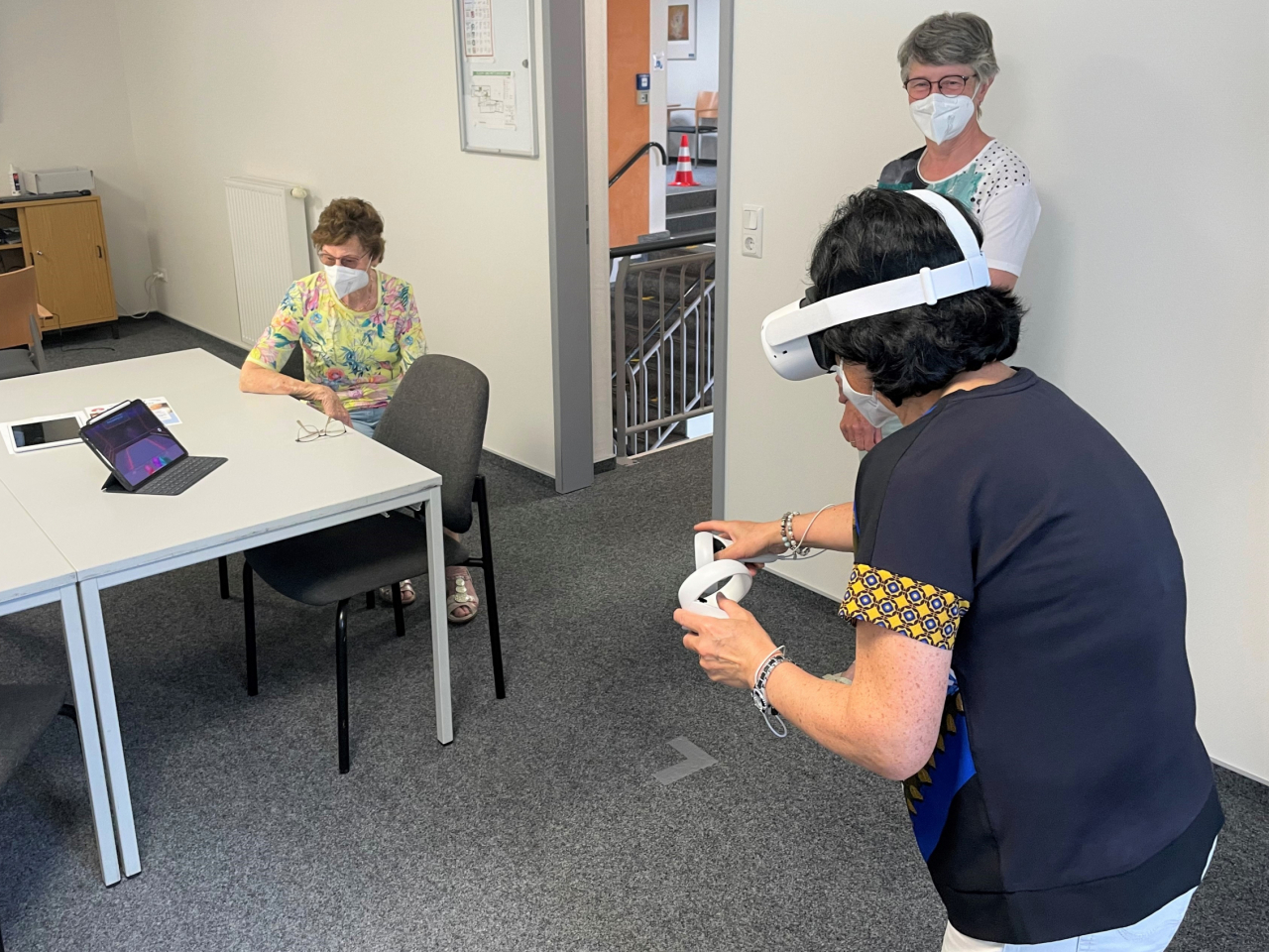 Frau spielt mit VR-Brille, zwei Frauen schauen zu