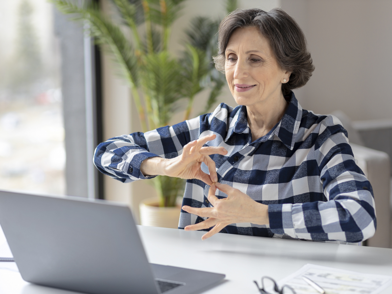 Deaf elderly woman uses sign language while video call using laptop while sitting in home office