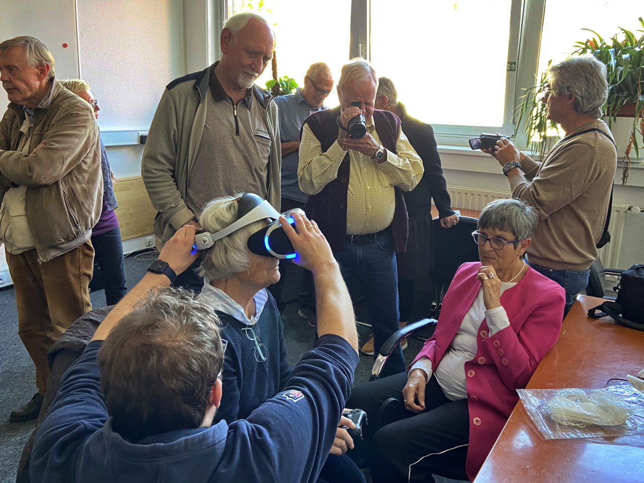 Eine Gruppe Menschen schaut sich verschiedene digitale Geräte an, darunter eine VR-Brillee